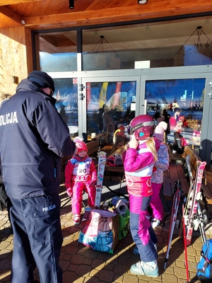 Policjant pozuje z dorosłym mężczyzną oraz dwójka dzieci, dzieci mają na rękach opaski odblaskowe.