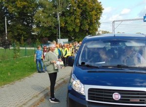 Uczennica w charakteryzacji ofiary wypadku drogowego przedstawiająca rysunek podróżującym na tle grupy młodzieży